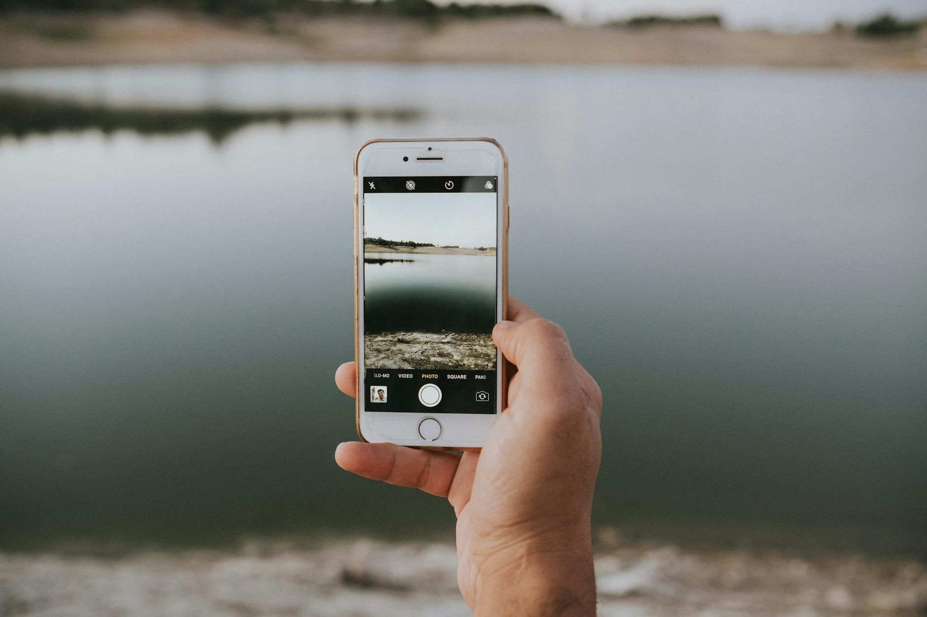 Person holding smartphone taking a photo outdoors with professional camera equipment in background