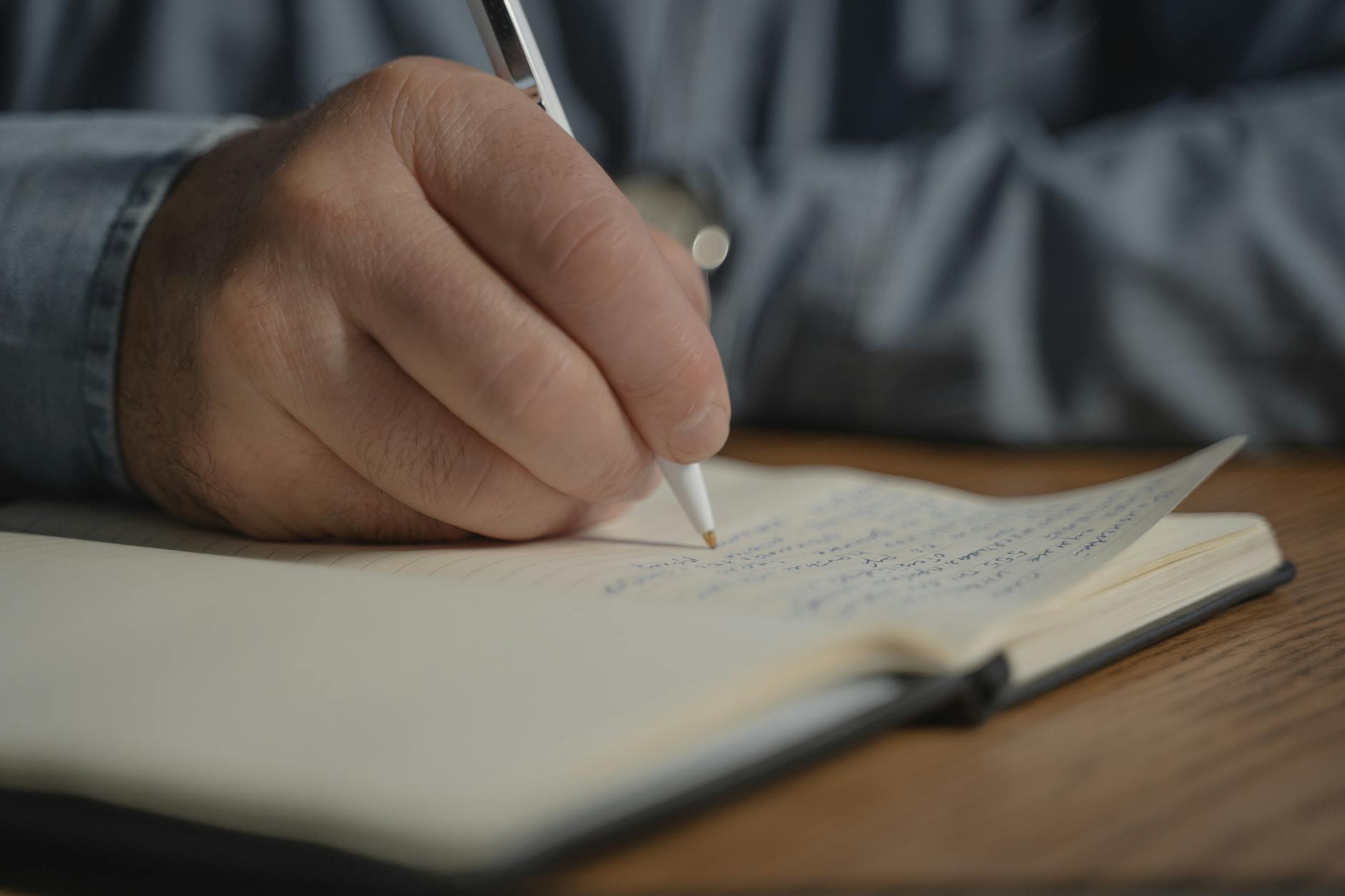 Person writing notes by hand in notebook with pen