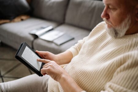 Kindle Rivals Worth Buying When Amazon Person holding an e-reader device while reading indoors