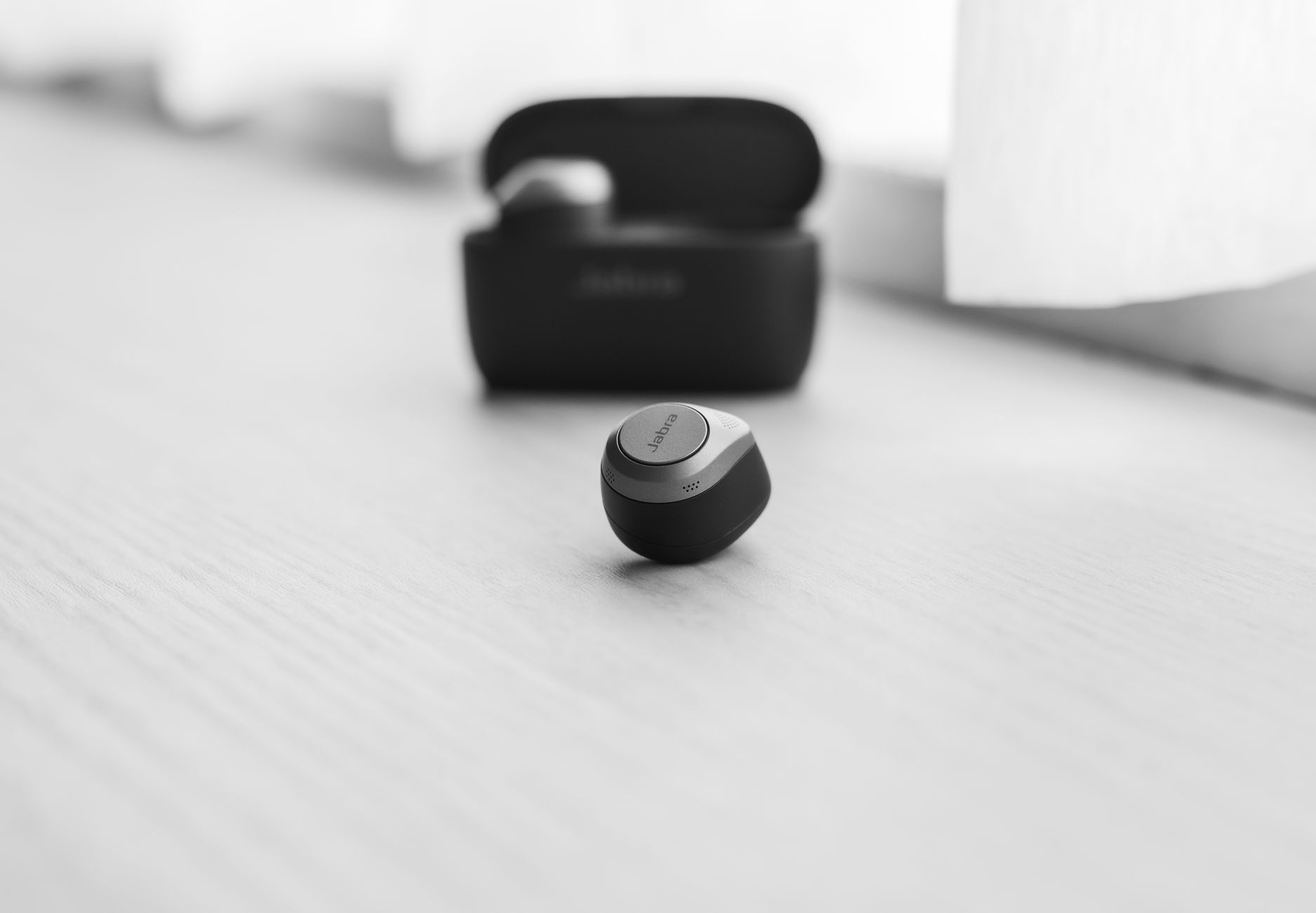 Wireless earbuds resting on a nightstand beside a bed