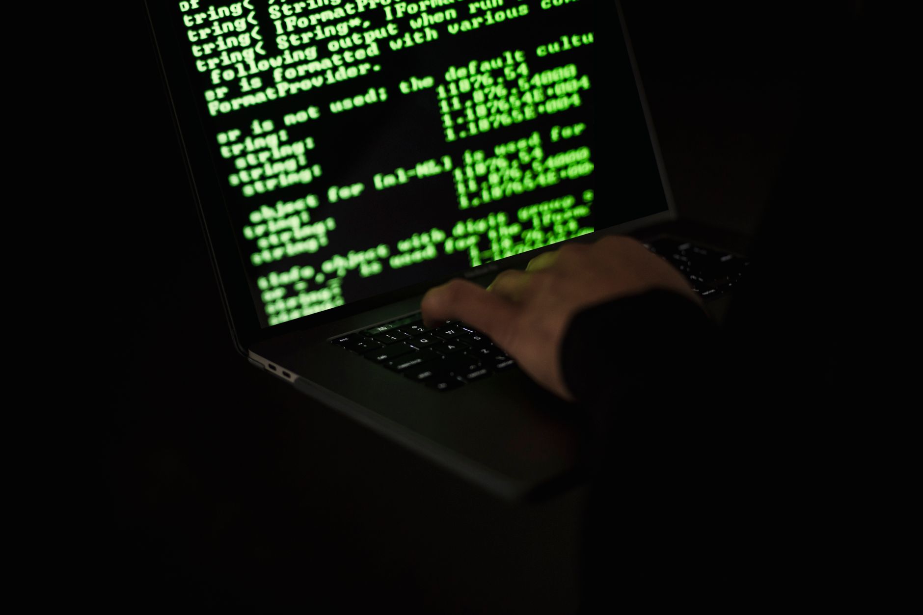Person at laptop in dark room representing cybersecurity threat and hacking activity