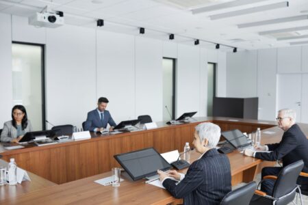 DeepMind CEO calls for an independent standards body to regulate frontier AI Business executives discussing regulatory policy in a formal boardroom setting