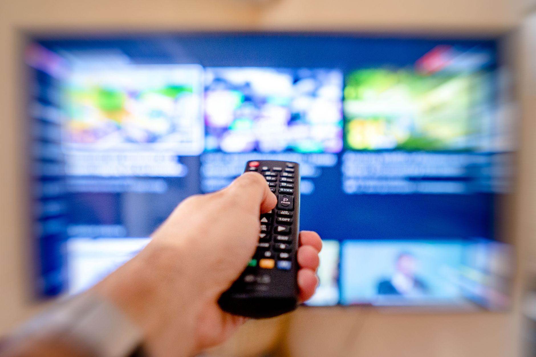 Person holding a remote control in front of a streaming TV screen