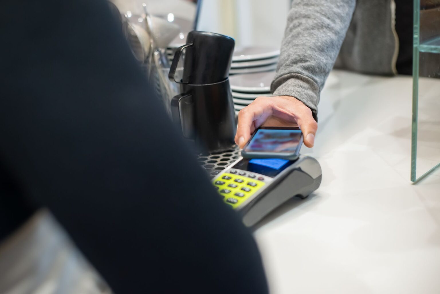 Person holding a smartphone near a contactless payment terminal