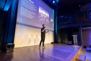 Speaker on stage at a technology conference with large screen display