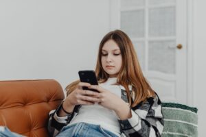 A teenage girl looking at her phone screen with a concerned expression